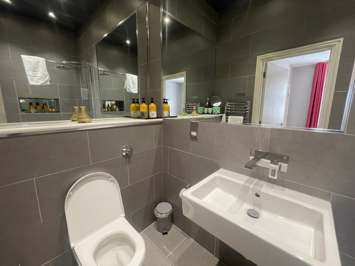 Hastings House Bedroom 7 ensuite — dark grey tiles, wall-hung basin and chrome heated towel rail